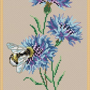 May include: Cross-stitch design of blue and purple flowers with green stems and leaves. A yellow and black bee is positioned near the flower. The background is a light tan color, and the image is framed in a light brown border.