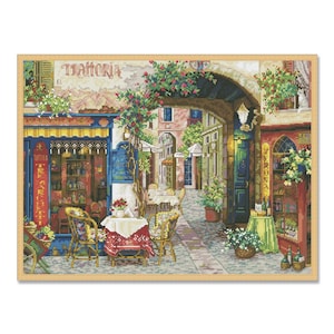 Peut inclure: Une broderie au point de croix colorée représentant une charmante scène de rue italienne avec un café, des tables, des chaises et une enseigne qui indique "Trattoria".