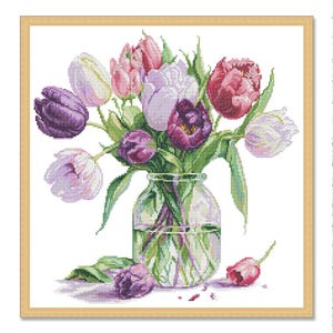 May include: A cross-stitch image of a bouquet of tulips in a glass jar. The tulips are in shades of purple, pink, and white, with green stems and leaves. The jar sits on a white background, with a few loose petals.