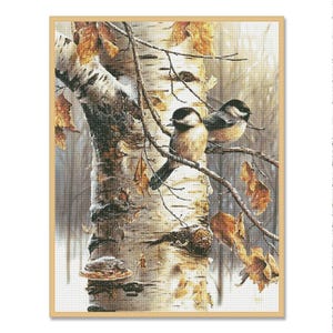 Puede incluir: Una impresión enmarcada de dos pequeños pájaros posados en una rama de árbol. Los pájaros tienen marcas negras y blancas. El tronco del árbol es blanco con marcas oscuras y hay hojas marrones. El fondo es una escena invernal borrosa.