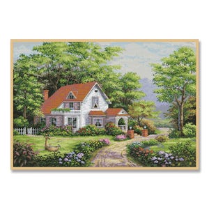 May include: A white house with a red roof and green trim sits on a grassy hill. The house has a porch with white railings and a white door. There are trees and bushes surrounding the house.