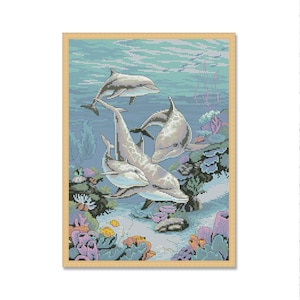 May include: A cross-stitch pattern featuring three dolphins swimming in a blue ocean with coral reefs and other sea life. The dolphins are gray and white, and the coral reefs are pink, orange, and green.