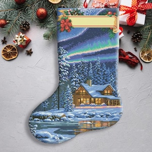 May include: A Christmas stocking featuring a winter scene with a cabin in the woods, a snowy landscape and a starry night sky. The stocking has a blank space for a name.