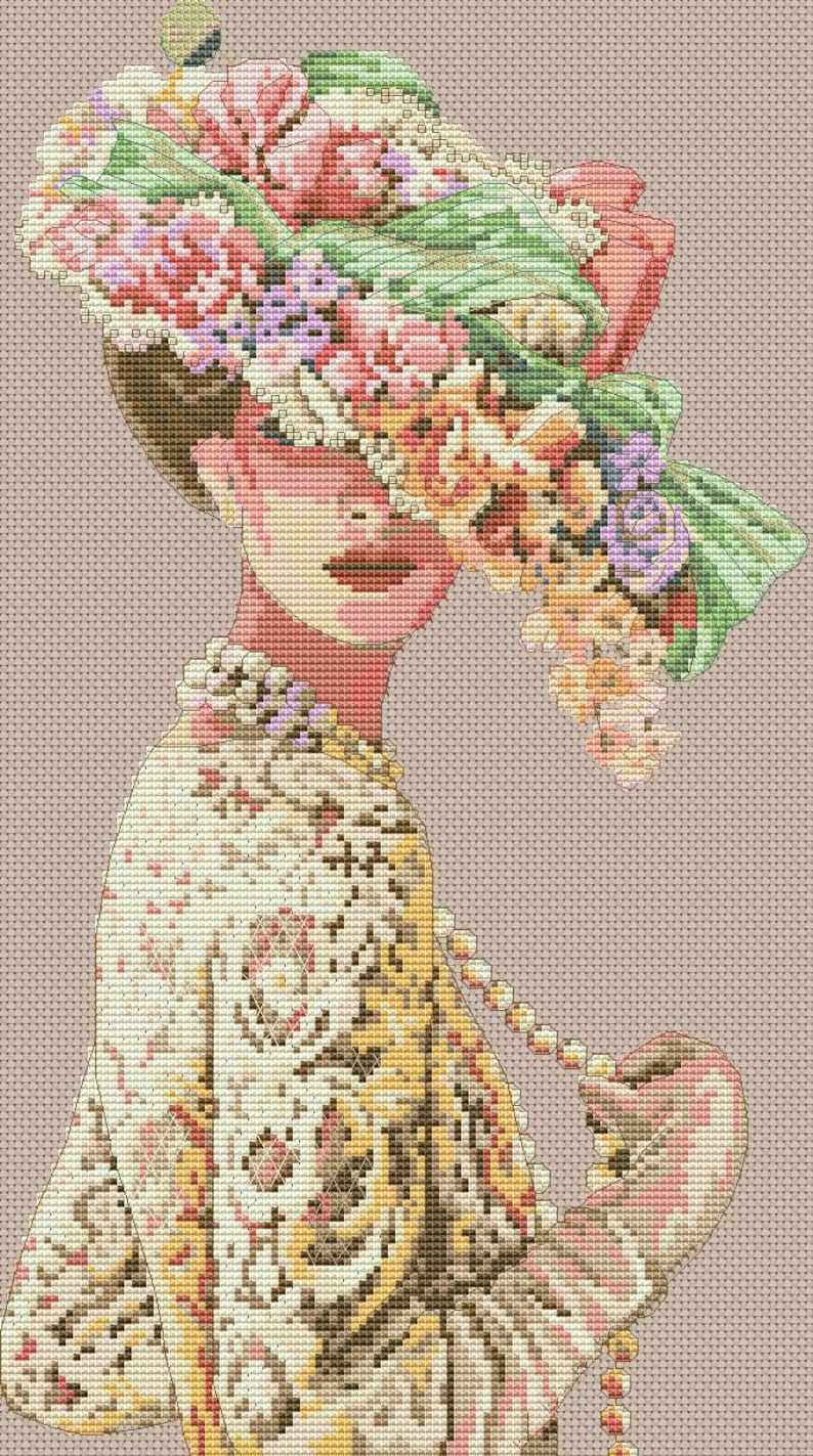 May include: A woman wearing a white dress with a floral pattern and a large hat adorned with pink, green, and purple flowers. She is holding a string of pearls in her hand.