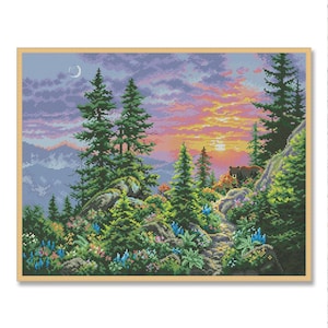 May include: A framed cross-stitch landscape showing a sunset over a mountain scene. The artwork features green pine trees, colourful wildflowers, and a small cabin. The sky transitions from purple to orange, with a crescent moon visible.