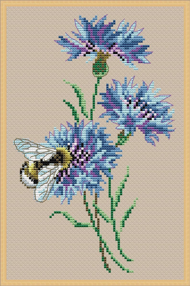May include: Cross-stitch design of blue and purple flowers with green stems and leaves. A yellow and black bee is positioned near the flowers. The background is a light tan color, and the image is framed in a gold border.