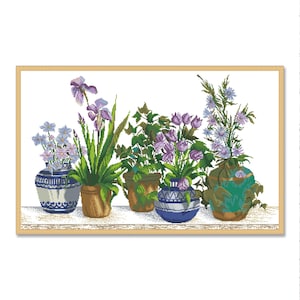 May include: A still life featuring five potted plants with purple and blue flowers in a variety of ceramic pots. The pots are decorated with blue and white patterns. The plants are arranged on a white surface with a light brown wooden frame.