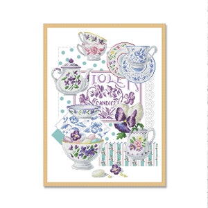 May include: A framed cross-stitch design featuring a teapot, cups, saucers, and a bowl filled with candy. The design is in shades of blue, purple, and white with a floral motif. The text "Violet Candies" is visible in the center of the design.