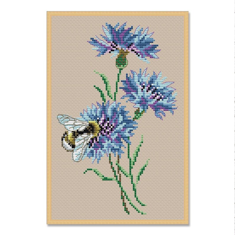 May include: Cross-stitch pattern of blue cornflowers with green stems and leaves, and a bee. The flowers have a detailed, textured appearance, with shades of blue and purple. The bee is yellow and black, with translucent wings. The background is a light tan.