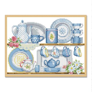 Könnte beinhalten: Kreuzstich-Kunstwerk mit einer Sammlung von blau-weißen Teetassen, Teekannen und Tellern, die auf Regalen angeordnet sind. Das Design umfasst florale Akzente und einen Holzrahmen. Die Farbpalette ist überwiegend blau und weiß mit Akzenten in Rosa und Gelb.