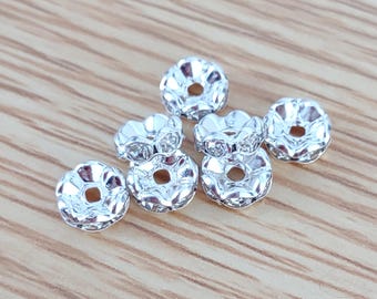 May include: Six silver-toned metal bead caps with clear rhinestones. The bead caps have a scalloped edge and a small hole in the center.