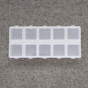 May include: A clear plastic storage box with 12 compartments. The box is empty and has a rectangular shape.