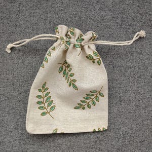 May include: A small, off-white drawstring bag with a green leaf pattern. The bag is made of a natural fabric and has a simple design.