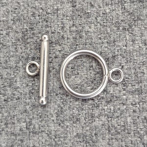 May include: Silver toggle clasp with a round ring and a straight bar with a rounded end. The clasp is a common jewelry finding used for necklaces, bracelets, and other jewelry.