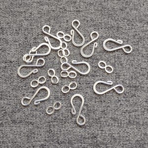 May include: A collection of silver-colored metal S-hooks and small figure-eight shaped jump rings. The S-hooks feature curved ends for connecting jewelry components, while the figure-eight rings are solid loops used for linking chains or charms.