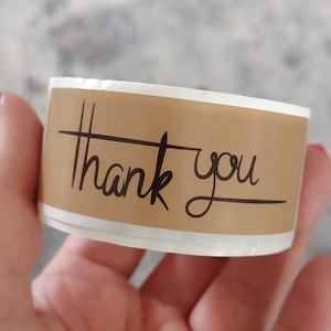 May include: A roll of brown kraft paper tape with a white label that says "thank you" in black script.