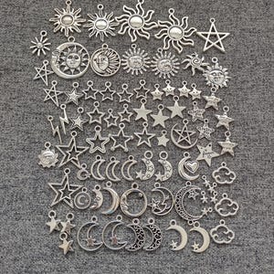 May include: A collection of silver-colored charms featuring celestial designs. The charms include suns, moons, stars, and clouds. The charms are of various sizes and styles, suitable for jewelry making or crafting.