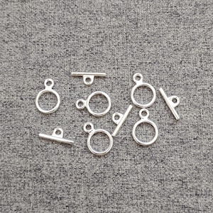 May include: A collection of silver-colored metal toggle clasps for jewelry making. Each set consists of a circular ring component with a small loop and a separate T-shaped bar component with a central loop, designed for fastening necklaces or bracelets.
