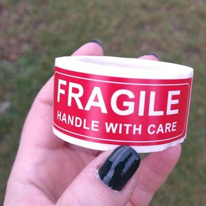 May include: A white roll of tape with a red label that says "FRAGILE HANDLE WITH CARE".