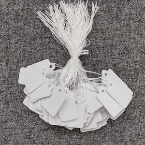 May include: A bundle of white string with white square tags attached. The tags have a hole punched in the top corner.