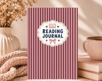 May include: A reading journal with a pink and brown striped cover. The cover features a white, scalloped-edged label with the words "READING JOURNAL" in navy blue, along with a book illustration, hearts, stars, and a bow. A pink mug and books are in the background.