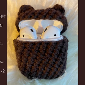 Könnte beinhalten: Eine braune, gehäkelte Hülle für AirPods in Bärenform. Der offene Fall zeigt weiße AirPods. Der Text "CROCHET PATTERN FOR AIRPOD-CASE GENERATION 1+2" ist sichtbar. Die Hülle liegt auf einer flauschigen, weißen Oberfläche.
