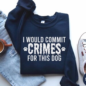 May include: A navy blue crewneck sweatshirt featuring white text that reads I WOULD COMMIT CRIMES FOR THIS DOG with two paw prints flanking the word CRIMES. The lettering has a dripping, melted effect, and the sweatshirt is displayed flat.