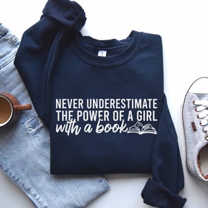 A navy color sweatshirt with the saying "Never underestimate the power of a girl with a book"