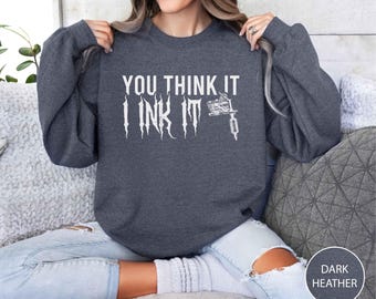 May include: Dark heather gray sweatshirt with the text "YOU THINK IT I INK IT" in white, along with a white tattoo machine graphic. The sweatshirt is a crew neck style.