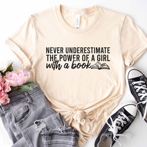 A natural color shirt with the saying "Never underestimate the power of a girl with a book"