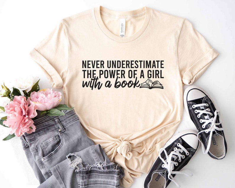 A natural color shirt with the saying "Never underestimate the power of a girl with a book"
