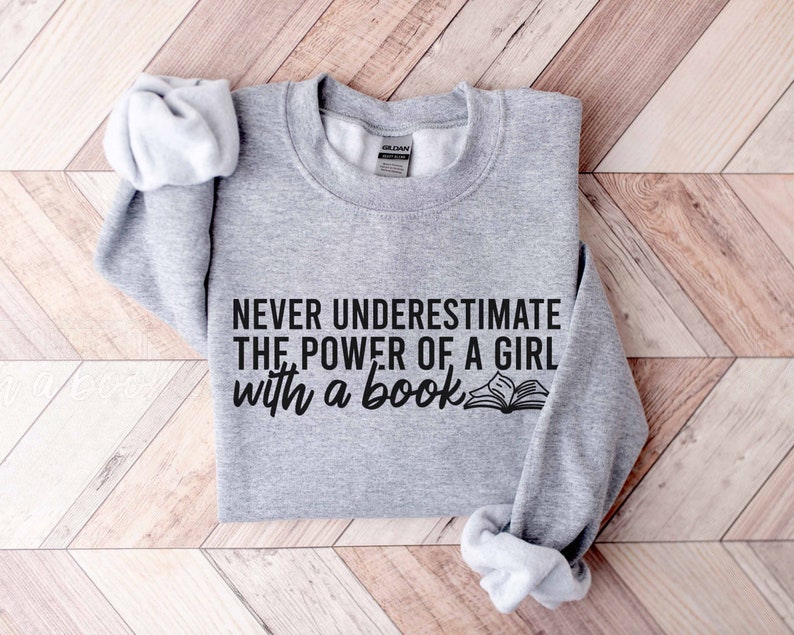 A sport grey color sweatshirt with the saying "Never underestimate the power of a girl with a book"
