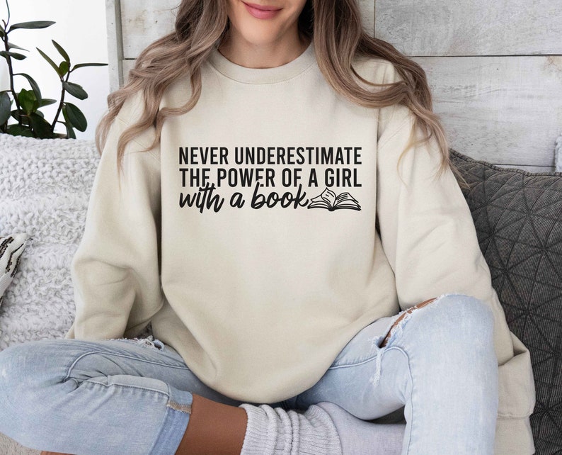A sand color sweatshirt with the saying "Never underestimate the power of a girl with a book"