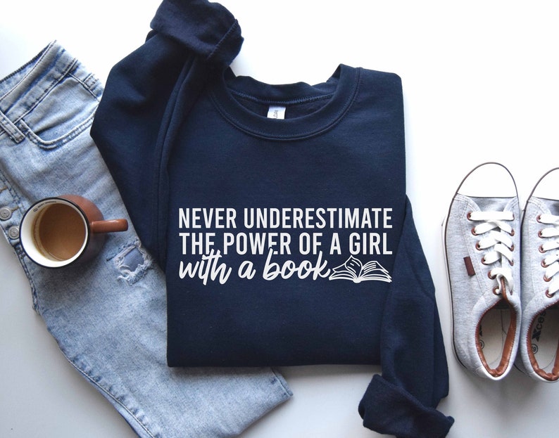 A navy color sweatshirt with the saying "Never underestimate the power of a girl with a book"