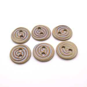 Puede incluir: Seis botones de cerámica con un patrón de espiral en tonos marrones y azules. Los botones tienen dos agujeros cada uno.