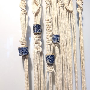 May include: A macrame plant hanger with four blue and white ceramic beads. The hanger is made of natural cotton rope and is designed to hold a small plant pot.