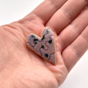 May include: A ceramic heart-shaped ornament with a purple and black abstract design.