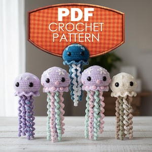 May include: A collection of five crocheted jellyfish in various colors, including purple, blue, and cream. Each jellyfish has a round head with black eyes and long, curly tentacles. The image includes a sign that says "PDF CROCHET PATTERN".