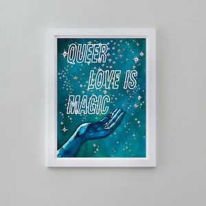 May include: A framed print with a blue background and white stars. The print features a hand reaching up with the text "QUEER LOVE IS MAGIC" in white.