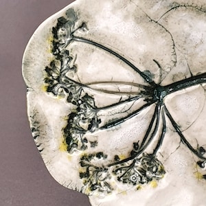 以下が含まれることがあります： 花が繊細にエンボス加工されたセラミック製の皿。皿は白地に黒と緑のアクセントが施されています。