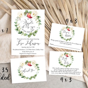 May include: A set of printable baby shower invitations with a watercolor wreath design featuring white flowers, green leaves, and a red apple. The invitations include a main invitation, a diaper raffle card, and a book request card. The text on the main invitation reads "The apple of my eye is on the way!" and includes the name "Lori Johnson". The diaper raffle card says "Diaper Raffle" and the book request card says "Books for Baby".