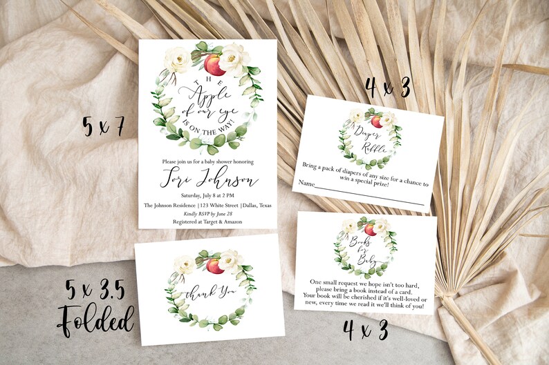 May include: A set of printable baby shower invitations with a watercolor wreath design featuring white flowers, green leaves, and a red apple. The invitations include a main invitation, a diaper raffle card, and a book request card. The text on the main invitation reads "The apple of my eye is on the way!" and includes the name "Lori Johnson". The diaper raffle card says "Diaper Raffle" and the book request card says "Books for Baby".
