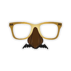 May include: A gold-colored plastic pair of glasses with a brown felt nose and black felt mustache. The glasses have the letters "HN" on the left side and "DU" on the right side.