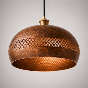 Pode incluir: Luminária pendente de cobre com textura martelada e uma faixa decorativa com padrão de losangos. A luminária tem uma parte superior de cor latão e um cabo preto. O interior da cúpula tem um brilho quente e dourado.