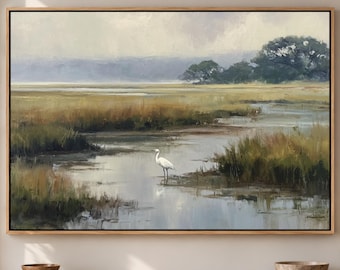 May include: A rectangular landscape painting in a light wood frame depicting a marshland scene with a white egret standing in shallow water. The artwork features muted tones of green, brown, and grey, with distant trees under a soft, overcast sky.