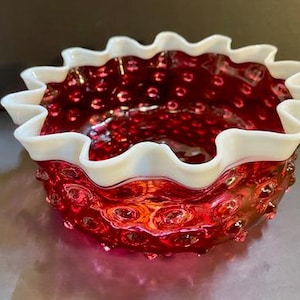 Könnte beinhalten: Eine rote Glasschüssel mit einem weißen, gewellten Rand und einer strukturierten, gepunkteten Oberfläche.