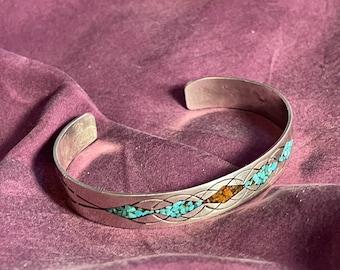 May include: A silver bracelet with a woven design and inlaid turquoise and orange stones.