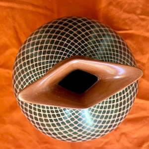 Puede incluir: Una olla de cerámica verde y marrón con un patrón geométrico y un pico de color cobre.