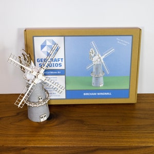 May include: A laser-cut model kit of a white and blue windmill with a brown base. The box shows a picture of the assembled windmill and the text "BIRCHAM WINDMILL".