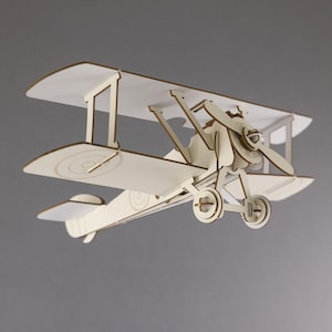 May include: A cream-colored biplane model with a propeller and two wings. The model has a detailed design, including the wheels and tail. The plane is made of wood and is set against a gray background.